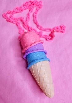 an ice cream cone necklace is on a pink surface with a chain attached to it