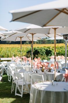 tables and chairs with umbrellas set up for an outdoor wedding reception in the sun