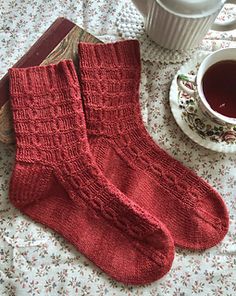 two red socks sitting on top of a table next to a cup of tea