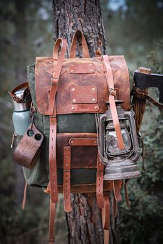 a leather backpack hanging from a tree in the woods with two cups and an umbrella