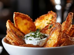 a white bowl filled with fried potato wedges covered in sour cream and parsley