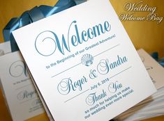 wedding welcome card with blue ribbon and bow on top of stack of folded cards that read, welcome to the beginning of our greatest adventure