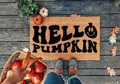 a person holding a basket of apples next to a door mat with the words hello pumpkin on it