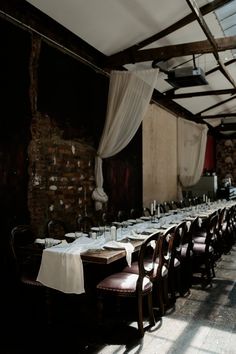 an empty dining room with long tables and white tablecloths on the tables in front of brick walls