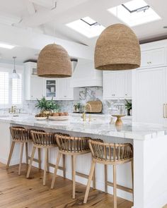 a kitchen with white cabinets and wooden stools in front of an island topped with marble counter tops