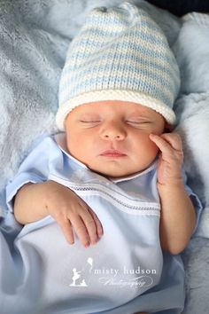 a newborn baby wearing a blue and white hat is sleeping on a blanket with his hands under his chin