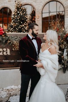 a bride and groom standing in front of a building with christmas lights on the windows