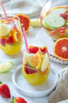 two glasses filled with fruit punch and garnished with strawberries, apple slices, and sliced oranges