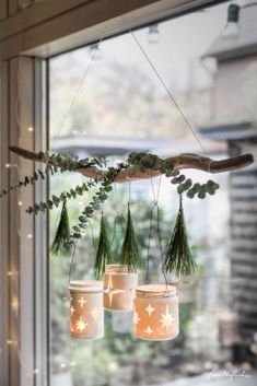 three mason jars are hanging from a branch with greenery and stars on them in front of a window