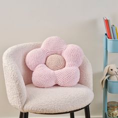 a pink flower shaped pillow sitting on top of a chair next to a book shelf