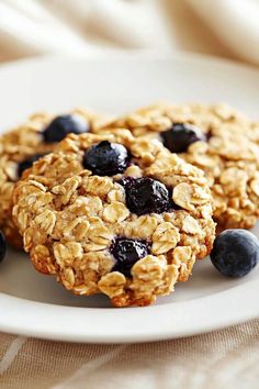 two blueberry oatmeal cookies on a white plate with fresh blueberries