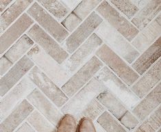 someone's feet are standing on the floor in front of a herringbone pattern