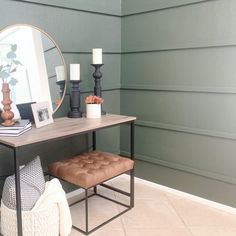 a table with a mirror, stool and candles on it in front of a green wall