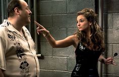 a man and woman standing in front of a brick wall pointing at something on the wall