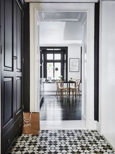 a black and white hallway with an open door leading to a dining room table in the background