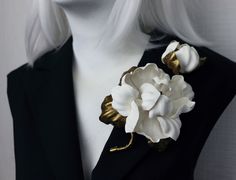 a woman with white hair wearing a black jacket and flower brooch on her lapel