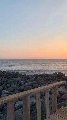 a wooden bench sitting on top of a rocky beach next to the ocean at sunset