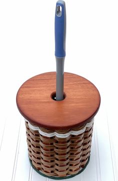 a wooden basket with a blue handle and a pen in it on a white surface