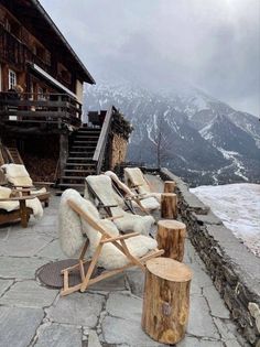 two lounge chairs sitting on top of a stone floor next to a wooden structure with snow covered mountains in the background