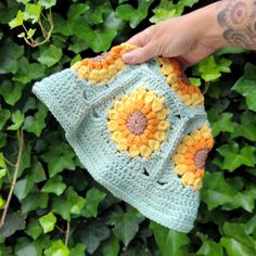 a hand holding a crocheted sunflower purse in front of some green leaves