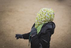 a young child with a yellow and green scarf on her head is pointing at something