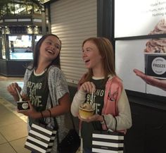 two girls standing next to each other and holding ice cream in front of a building