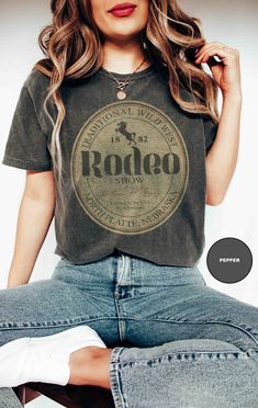 Well, howdy there, y'all! Welcome to the heart of the Wild West with our Traditional Wild West Rodeo Tee - a slice of cowboy culture that's as classic as a campfire under the stars! Let me tell ya about this tee - it's not just any ol' shirt; it's printed on genuine Comfort Colors® 1717 tees, y'all! And let me tell ya, these tees are softer than a tumbleweed rollin' through the prairie, with that vintage look and feel that'll make ya feel like you've stepped right out of a saloon from yesteryear Wild West Shirt, Retro Crew Neck Tops For Western-themed Events, Retro Western Style Short Sleeve Top, Vintage Crew Neck Top For Rodeo, Retro Letter Print Tops For Rodeo, Vintage Letter Print Tops For Western-themed Events, Vintage Short Sleeve Tops For Western-themed Events, Vintage Letter Print Tops For Rodeo, Retro Letter Print Top For Concerts