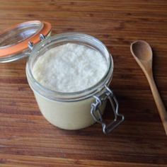 a wooden table topped with a glass jar filled with white liquid next to a spoon