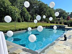 an outdoor pool with balloons floating in the air and a cat sitting next to it