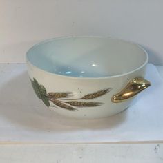 a white bowl with gold handles and wheat design