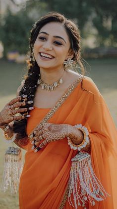 a woman in an orange sari smiles at the camera while holding her hands together