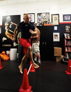 a man is jumping over orange cones in a room with pictures on the wall behind him