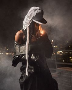 a woman wearing a white hat and black dress is standing in the dark with her hands on her hips