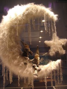 a display case with white feathers hanging from it's sides and two figurines in the middle