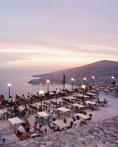 people are sitting at tables on the rocks by the water with lights in front of them