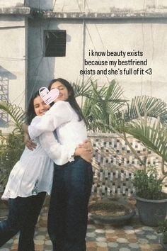 two women hugging each other in front of a building with plants and potted trees