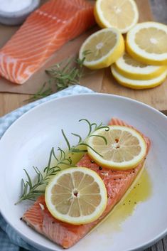 two pieces of salmon on a plate with lemons and rosemary