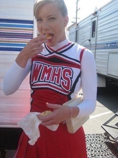 a woman in a cheerleader uniform eating food next to a campervane