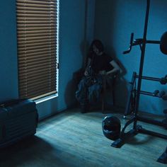 a woman sitting in a dark room next to a window with blinds on the windowsill