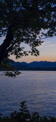 the sun is setting over water with mountains in the background