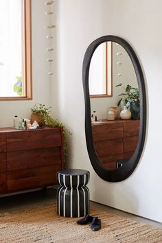 a large oval mirror sitting on top of a wooden dresser next to a black and white stool