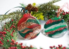 two christmas ornaments sitting on top of a table next to evergreen branches and pine cones