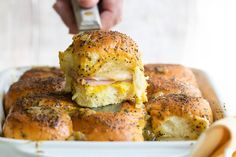 someone is taking a piece of ham and cheese sliders out of the casserole dish