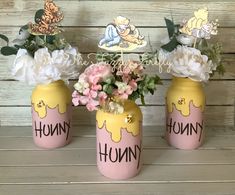 three painted jars with flowers in them sitting on a wooden table next to each other