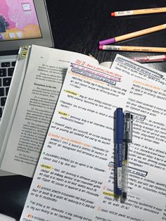 an open book next to a laptop computer and several pencils on top of it