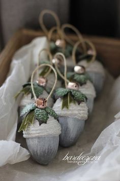 three silver acorns with green leaves and pink berries on them sitting in a basket