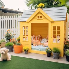 a small yellow dog house sitting on top of a lush green field next to potted plants