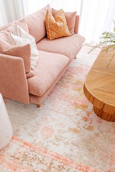 a living room with pink couches and pillows on top of the rug in front of a window