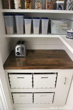 an organized pantry with white cabinets and wooden counter tops, including a toaster oven