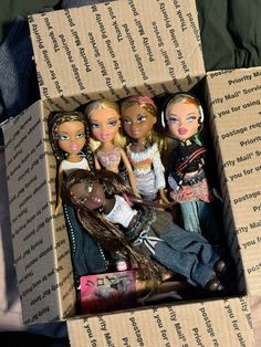 four dolls are in a cardboard box on the bed